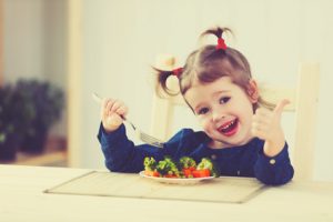 happy child girl loves to eat vegetables and showing thumbs up